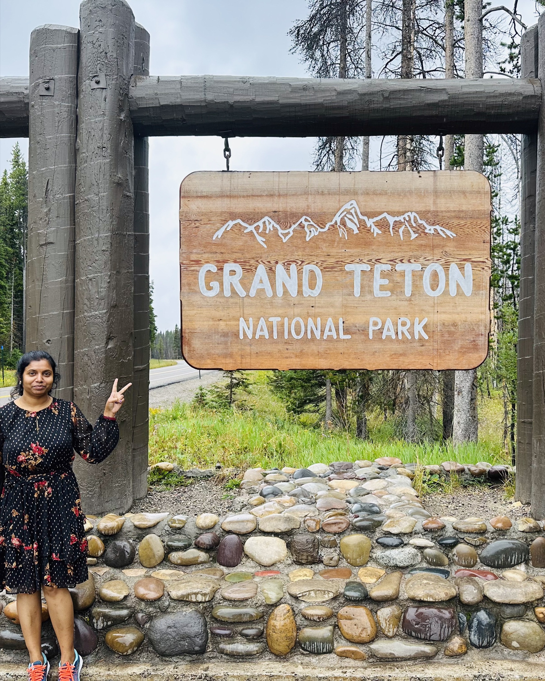 A traveler standing beside the Grand Teton National Park entrance sign
