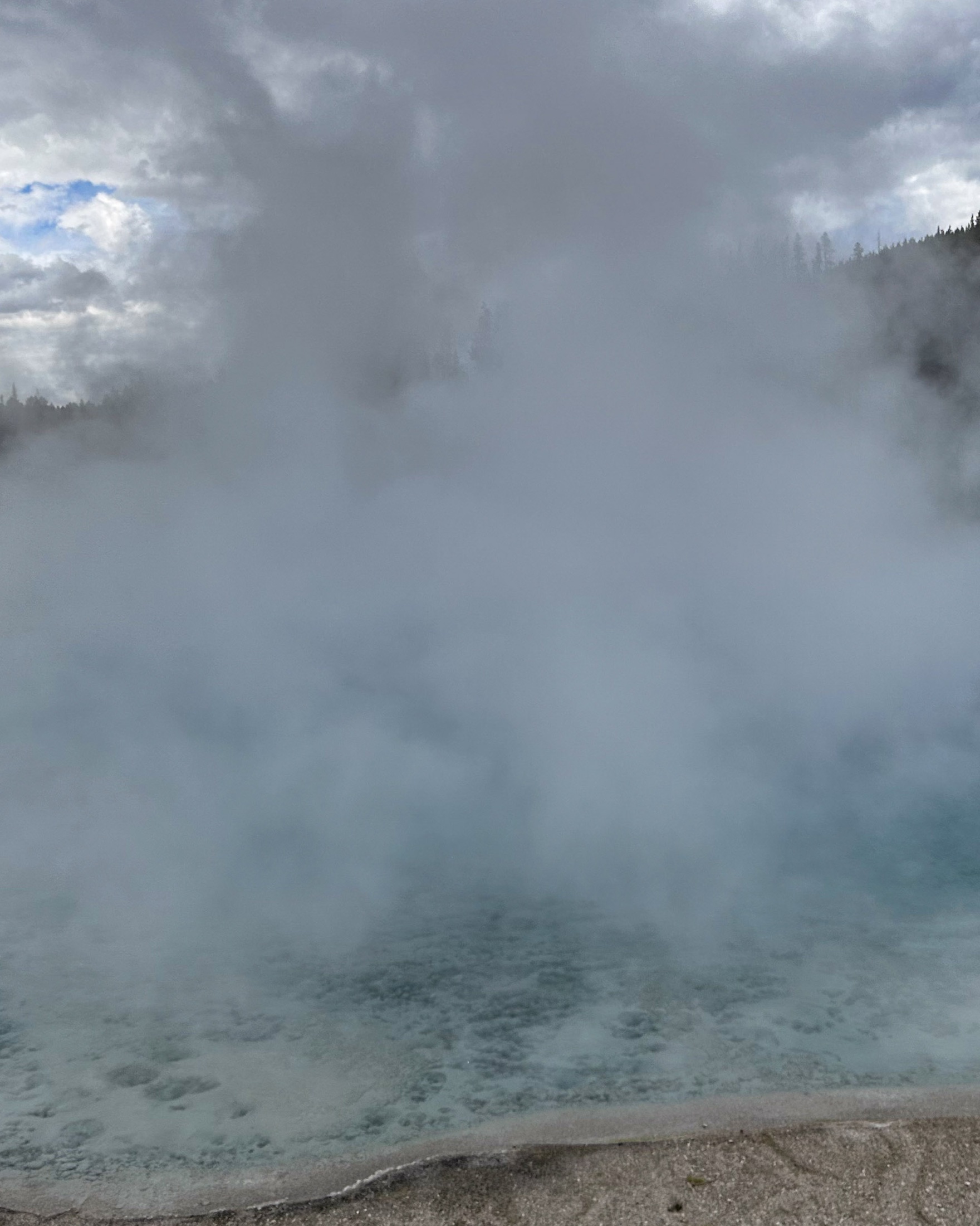 Dense steam rising above a pale blue geothermal pool
